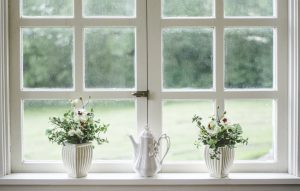 A teapot between two vases of flowers on a window sill