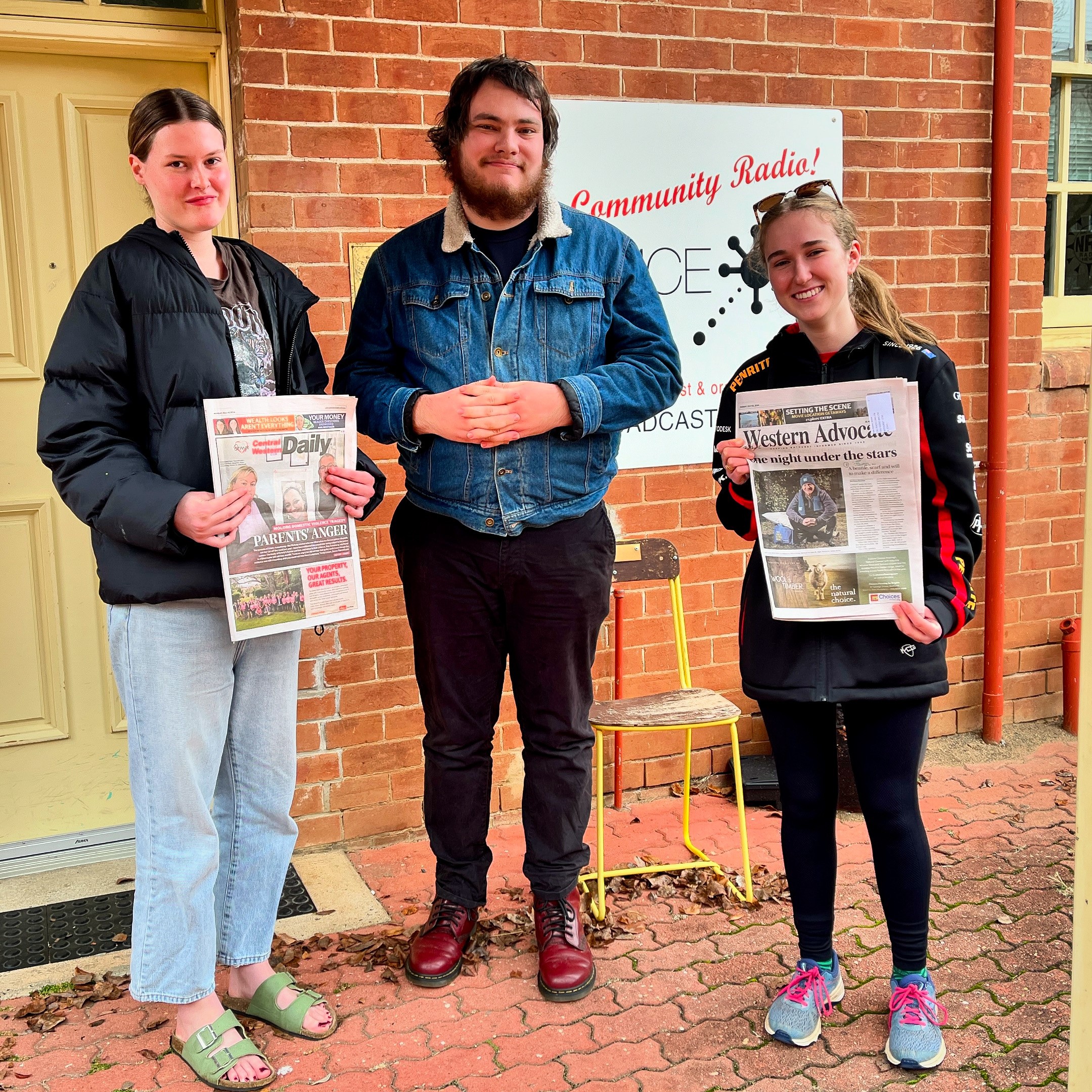 Two young women holding newspapers with a young man standing between them