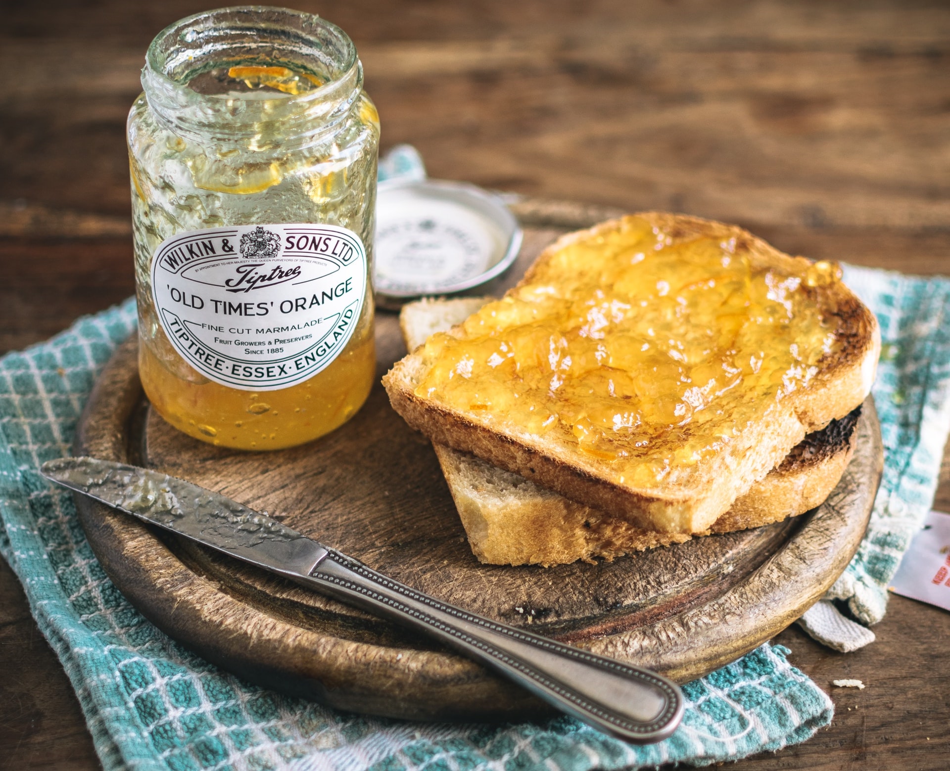 An open jar of marmalade sitting next to two pieces of toast and a butter knife
